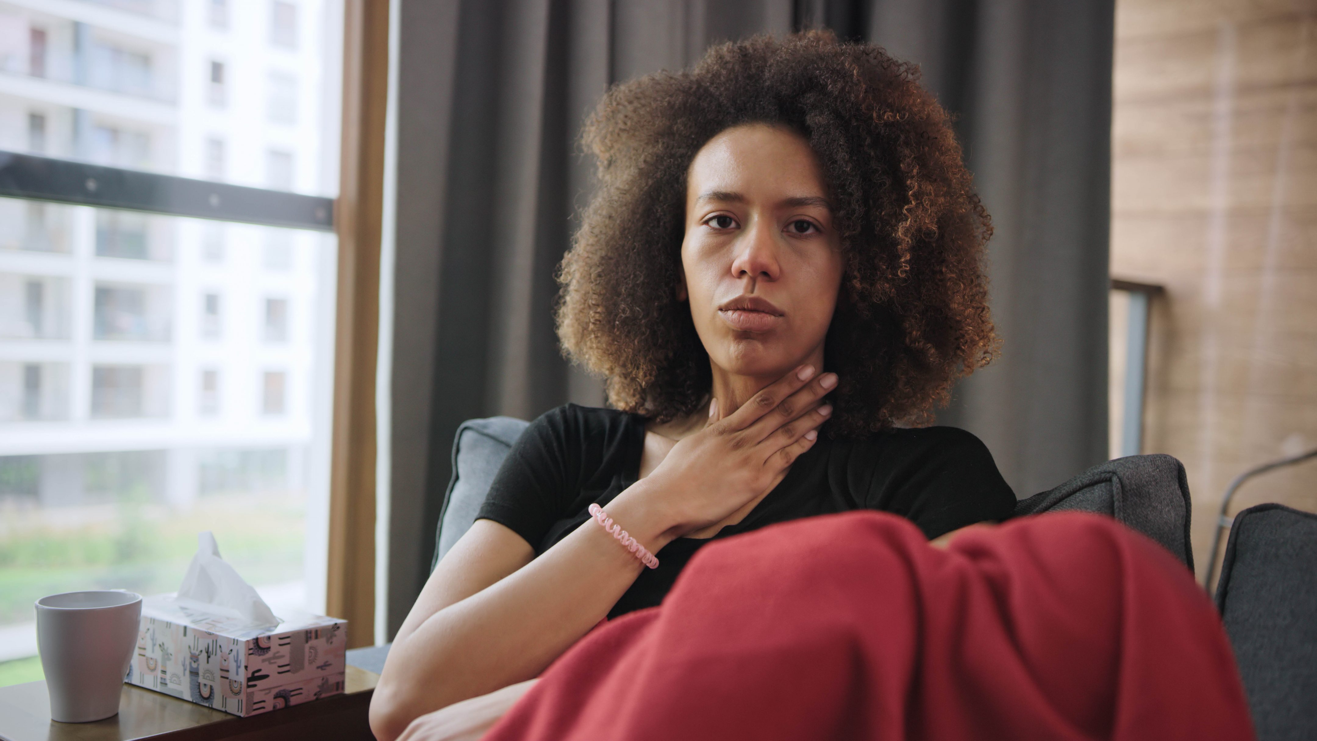 Sickly young woman staying on a couch. Having sore throat