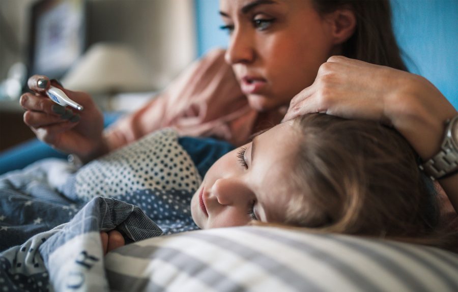 Child laying down sick with mom comforting